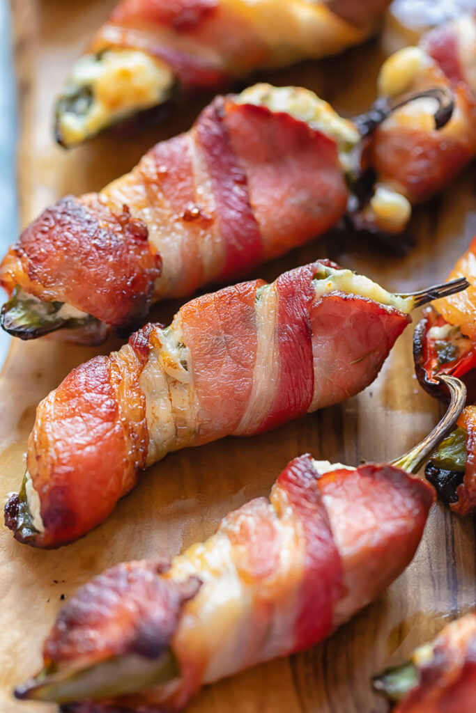 close up of three bacon wrapped jalapeno poppers on a wooden board