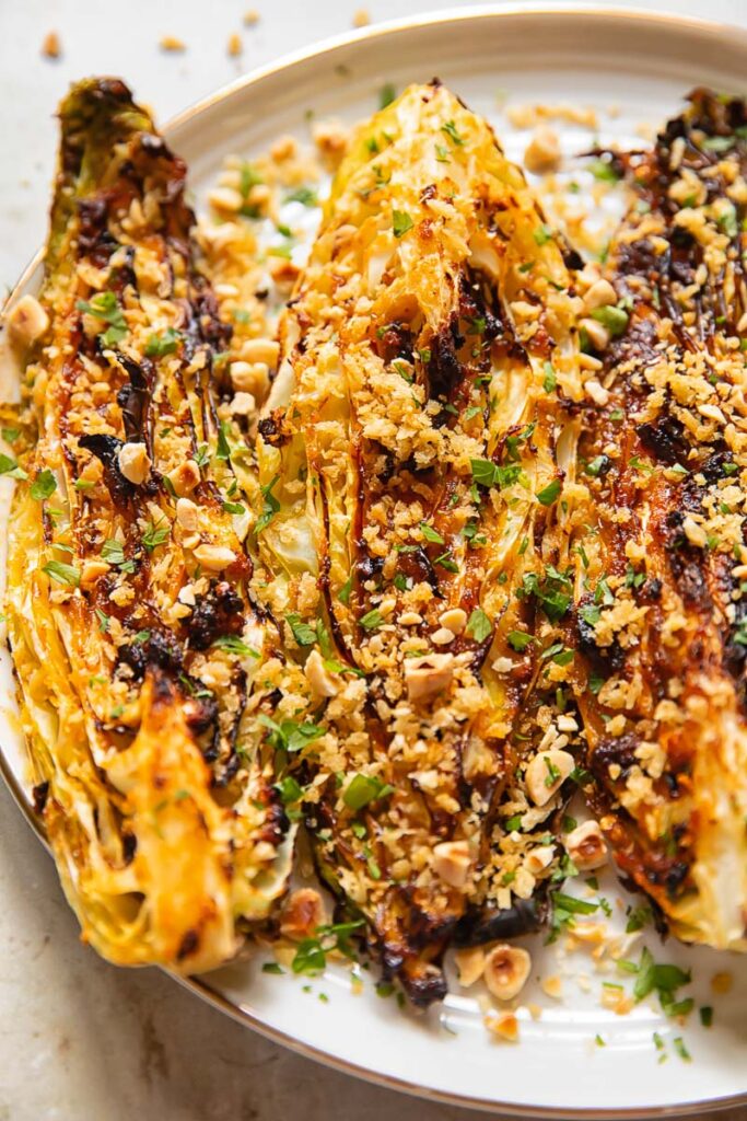 roasted cabbage wedges covered with herbs and chopped nuts, on a white plate