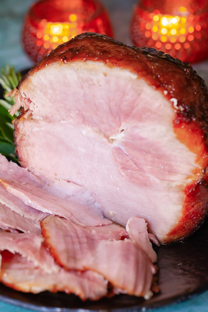 a glazed ham with pieces cut and a festive table in the background
