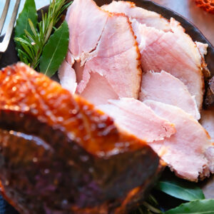 slices of glazed ham shown from the top down in a festive setting, with the glazed ham in the foreground