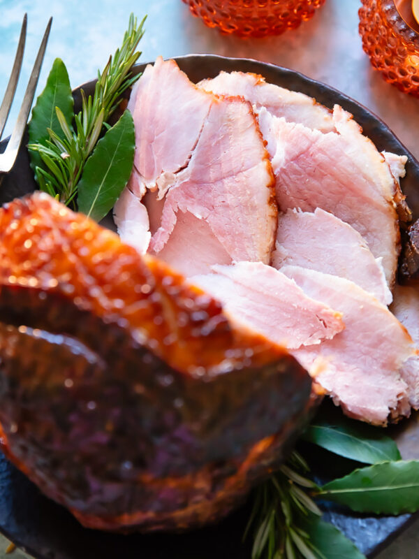 slices of glazed ham shown from the top down in a festive setting, with the glazed ham in the foreground