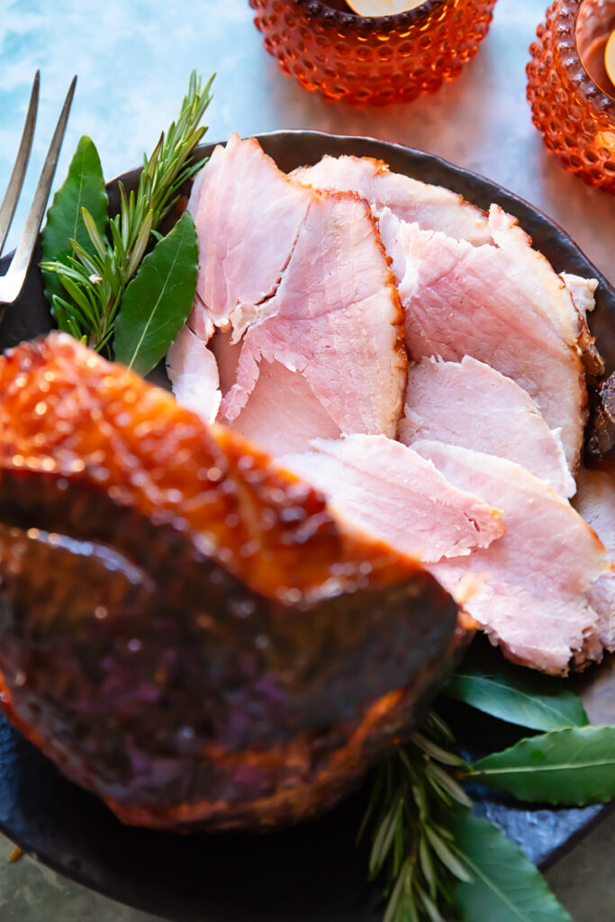 slices of glazed ham shown from the top down in a festive setting, with the glazed ham in the foreground