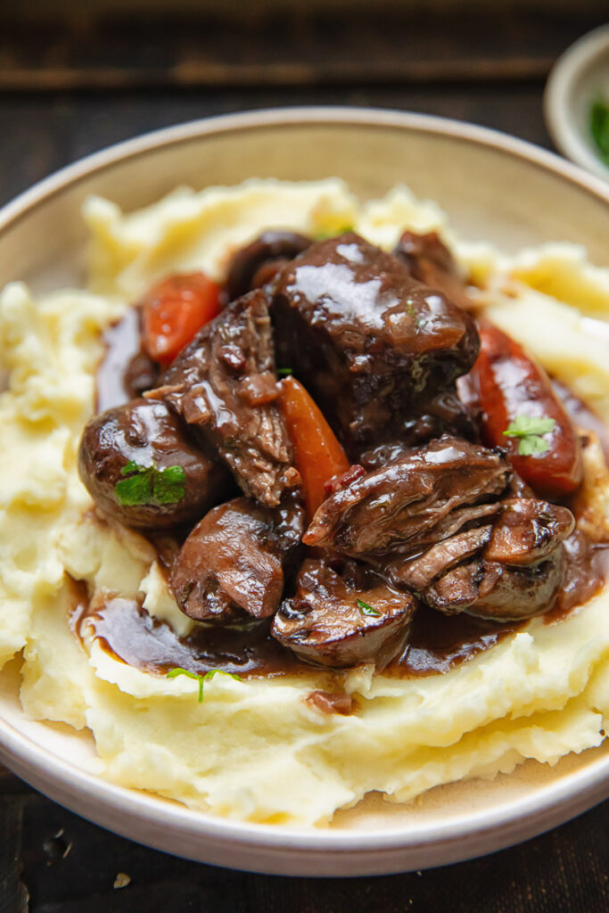Close up of short rib bourguignon on mashed potatoes in a bowl