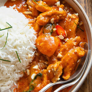 close view of curry in a bowl next to a ball of rice, with a spoon and fork