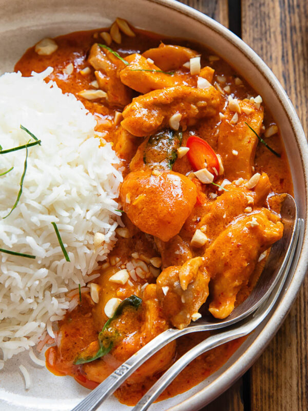 close view of curry in a bowl next to a ball of rice, with a spoon and fork