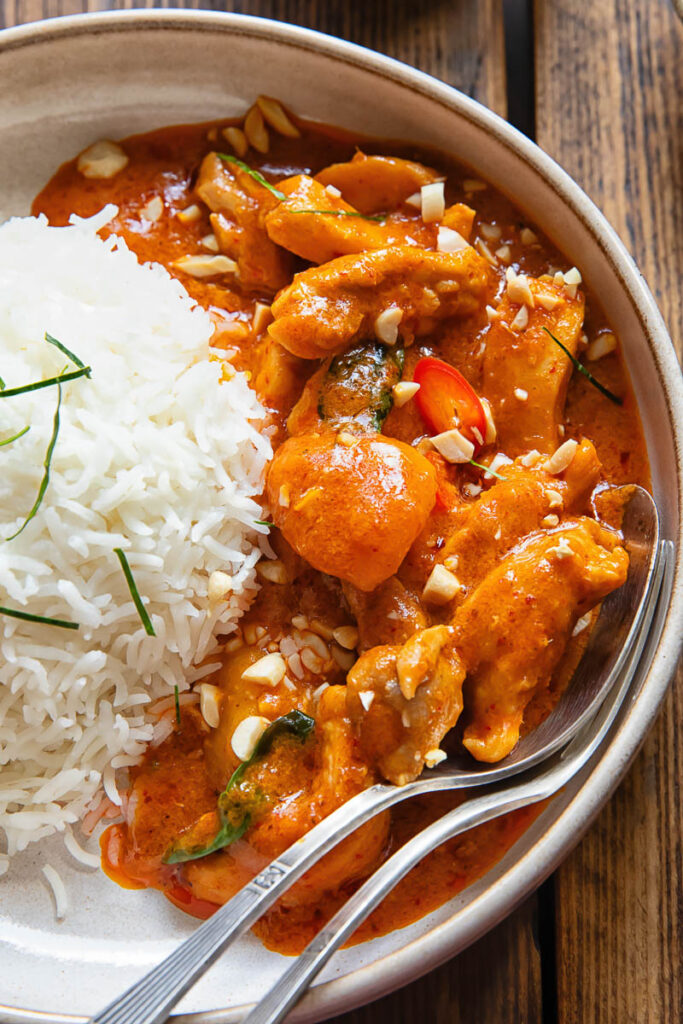 close view of curry in a bowl next to a ball of rice, with a spoon and fork
