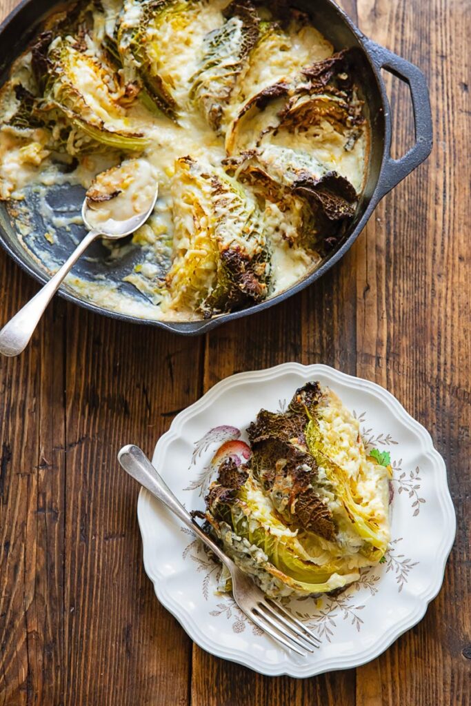 Savoy cabbage gratin in a skillet, and with a piece removed to a side plate, on a wooden background.