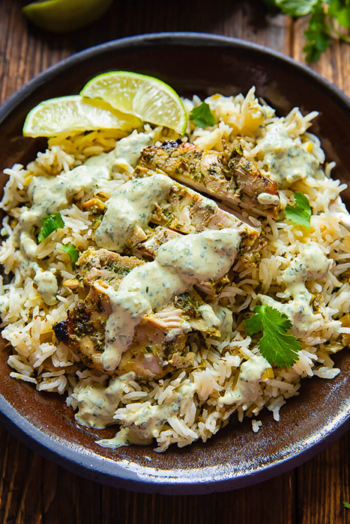 sliced cilantro lime chicken breast on top of rice with a sauce drizzled on 