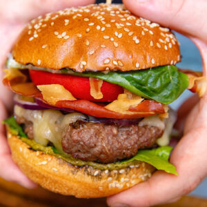 A vertical shot of a beef patty, tomato, lettuce and prosciutto in a bun in hands