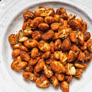 A pile of spiced butter beans on a white plate against a wood background.