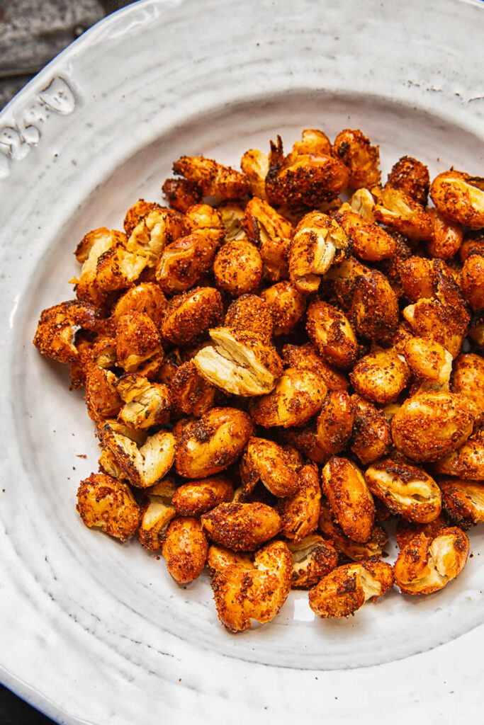 A close up image of cooked butter beans with orange spice on a rustic white plate.