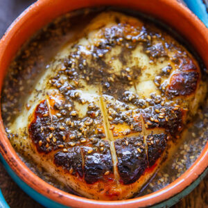 A chunk of baked halloumi in a small dish with the hot honey sauce on a wood background.