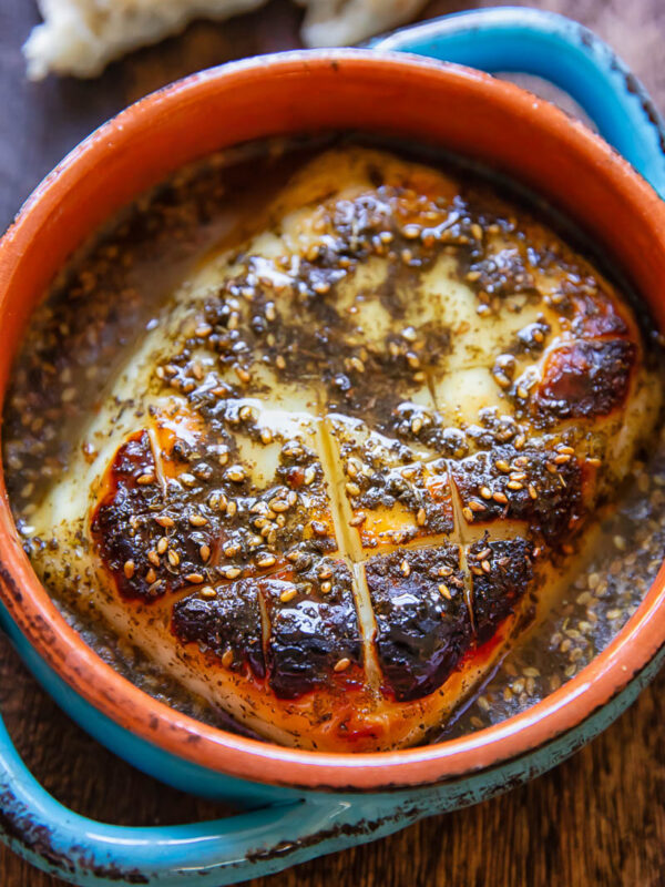 A chunk of baked halloumi in a small dish with the hot honey sauce on a wood background.