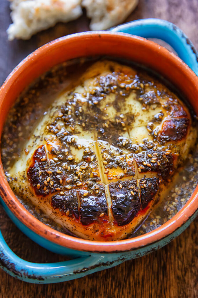 A chunk of baked halloumi in a small dish with the hot honey sauce on a wood background.