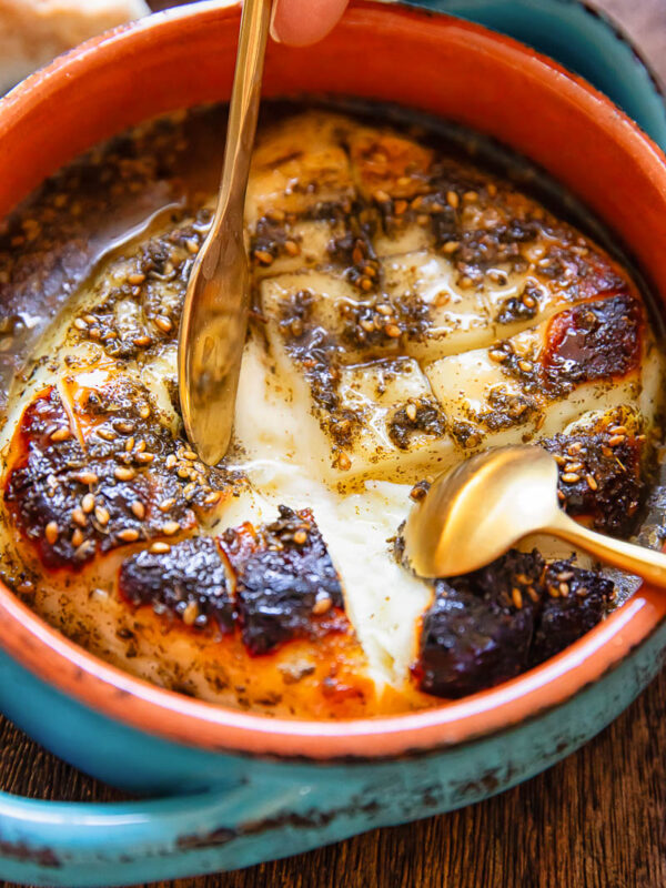 Close up of a small baking dish with baked halloumi being pulled apart by two small spoons.