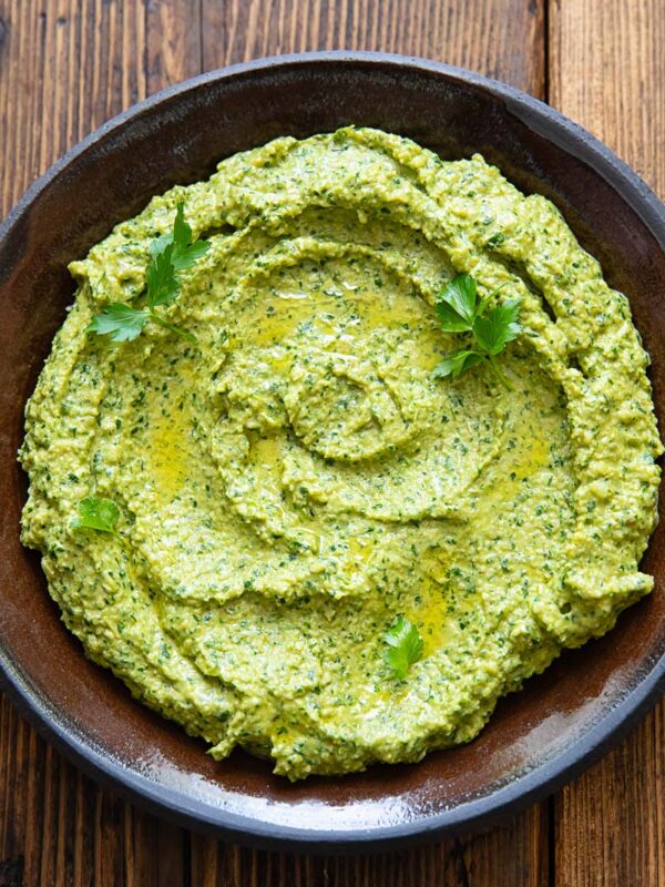 Green romesco sauce with herbs spread on a dark plate with a wooden background.