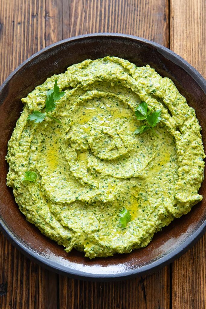 Green romesco sauce with herbs spread on a dark plate with a wooden background.