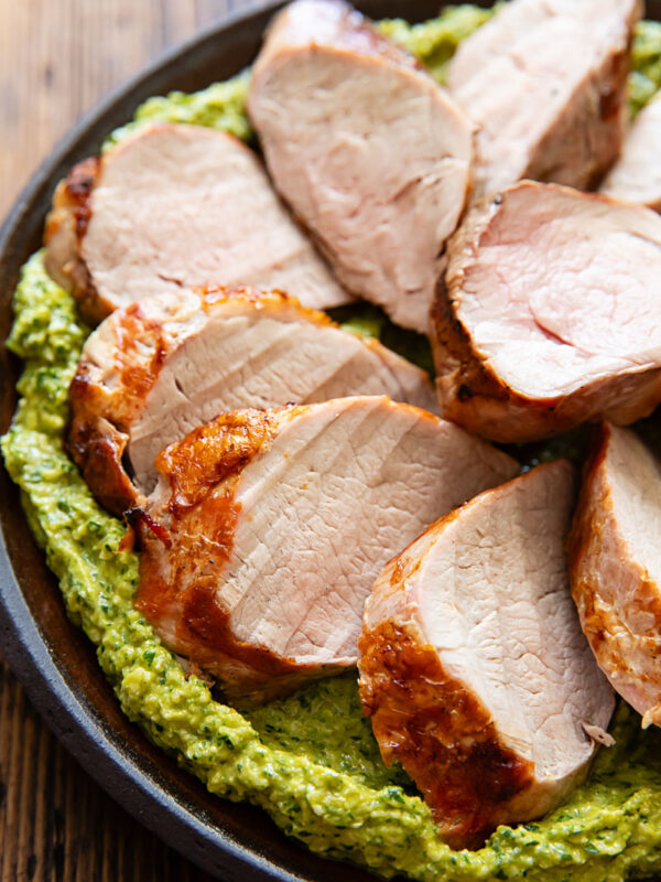 Close up image of pork tenderloin with green romesco on a dark plate.