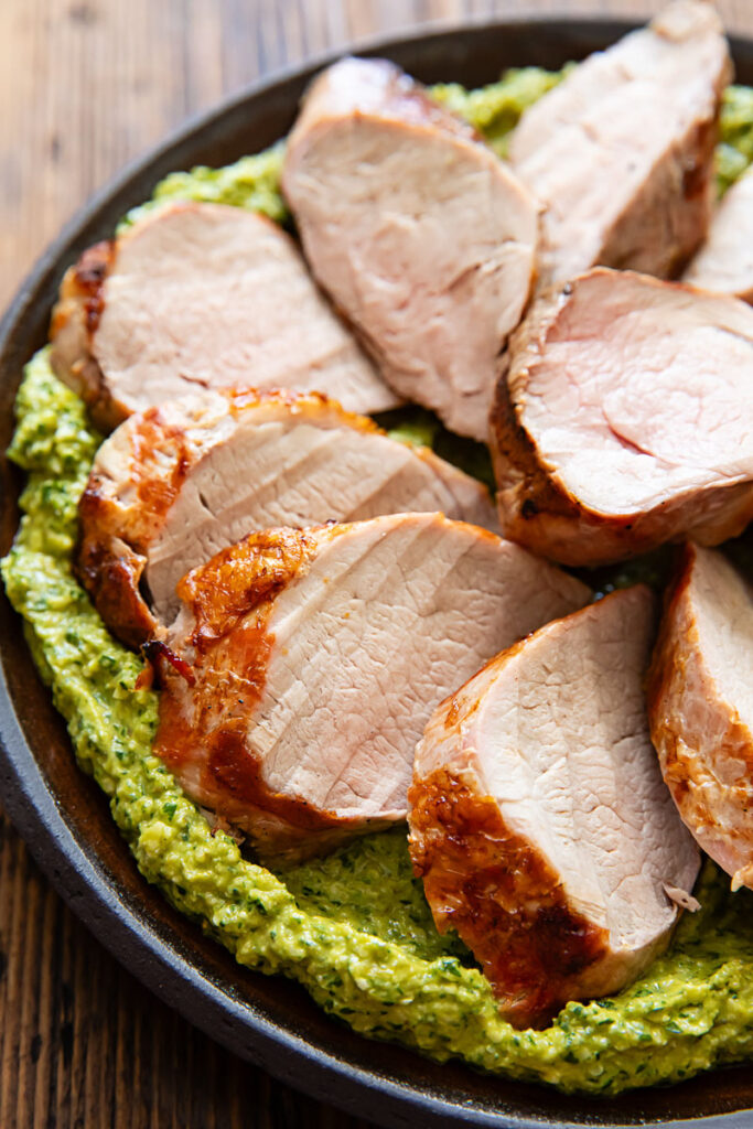 Close up image of pork tenderloin with green romesco on a dark plate.