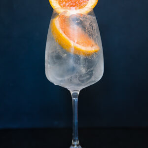 Image of a wine glass with a light coloured liquid with two slices of grapefruit.