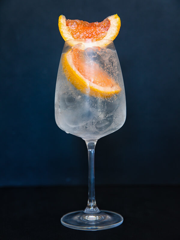 Image of a wine glass with a light coloured liquid with two slices of grapefruit.