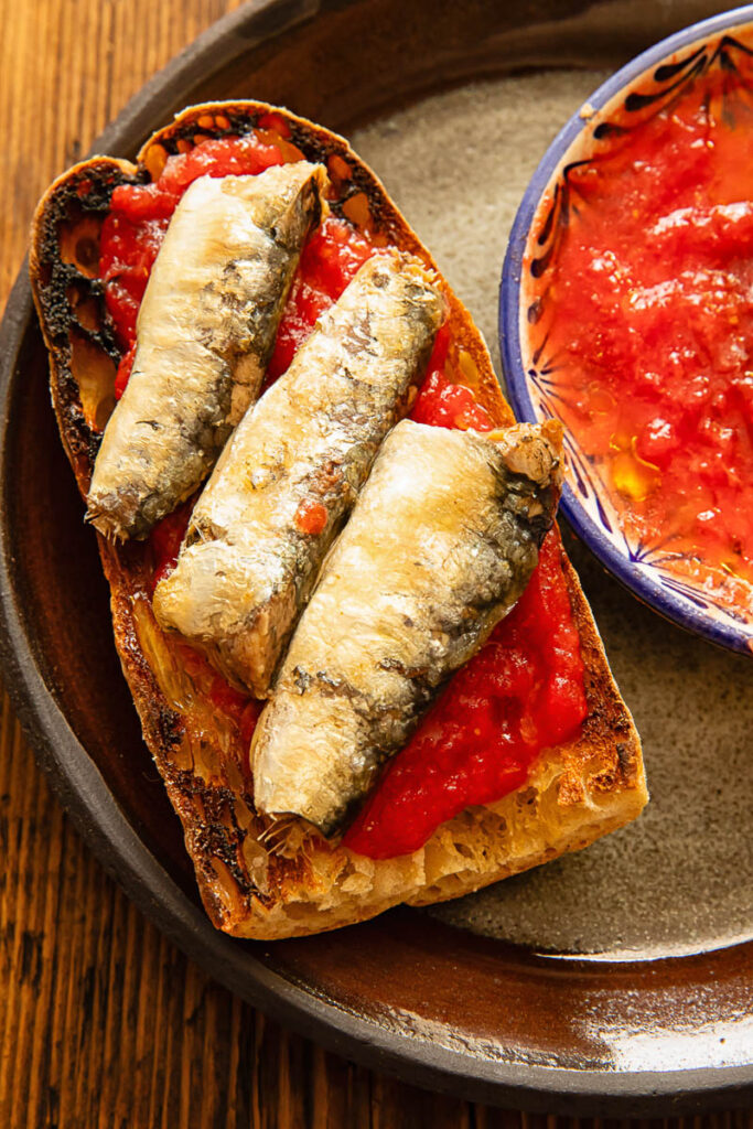 A dark plate with toast, sardines and tomato mixture.