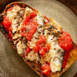 Toast on a dark plate with sardines and tomatoes.