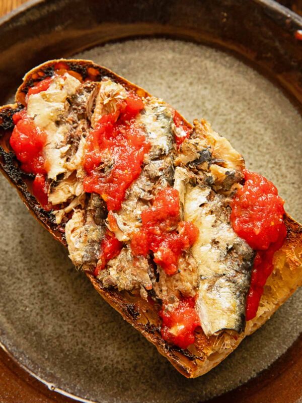 Toast on a dark plate with sardines and tomatoes.