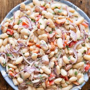 Top down photo of the bean salad in a white bowl on a dark wood background.