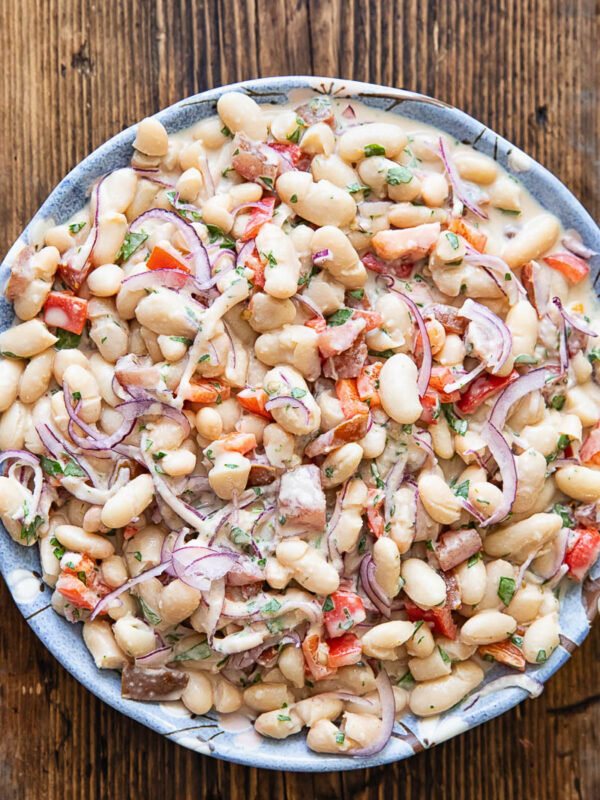 Top down photo of the bean salad in a white bowl on a dark wood background.