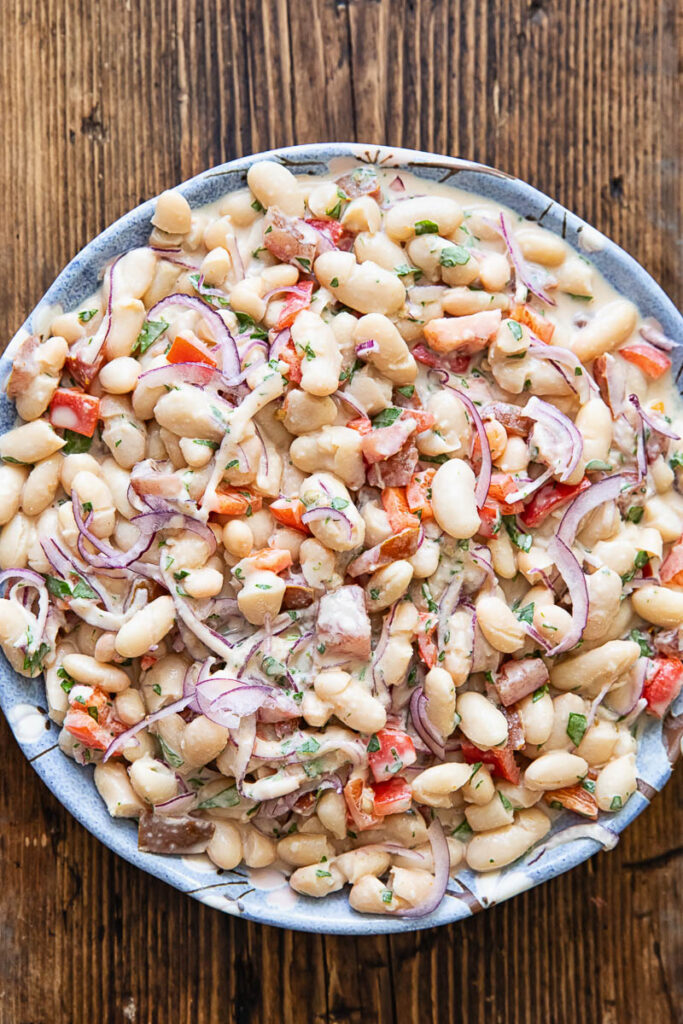 Top down photo of the bean salad in a white bowl on a dark wood background.