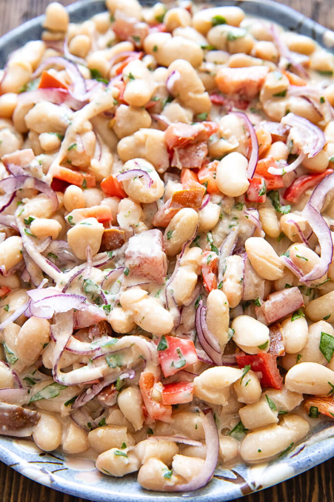 close up photo of the salad showing beans, onions and peppers with herbs and a creamy dressing.