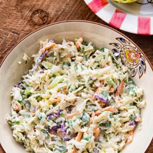 Close up of slaw in a bowl on a wooden background, next to a colourful plate with a lime half.