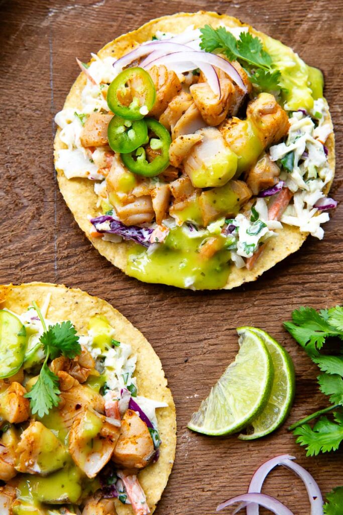 Top down view of two tostadas topped with white fish and a range of toppings on a wooden background.