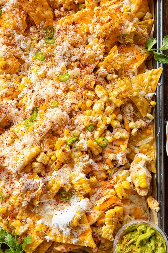 Close up of a baking sheet with nachos, with corn, jalape&ntilde;os, corn and Tajin seasoning.