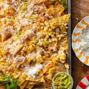 Close up of a corner of a baking sheet with nachos against a wooden background.