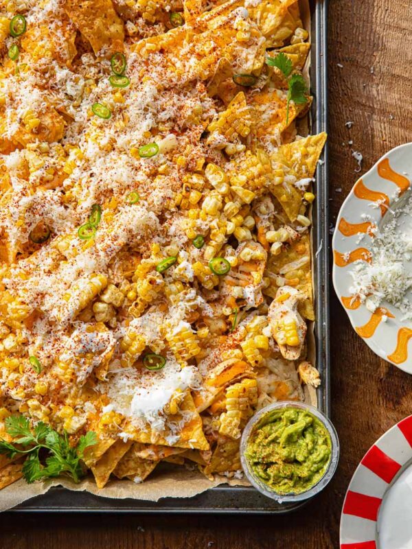Close up of a corner of a baking sheet with nachos against a wooden background.
