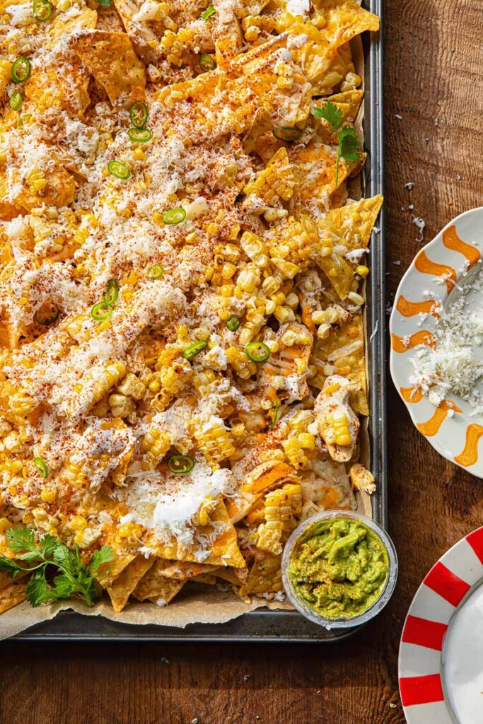 Close up of a corner of a baking sheet with nachos against a wooden background.